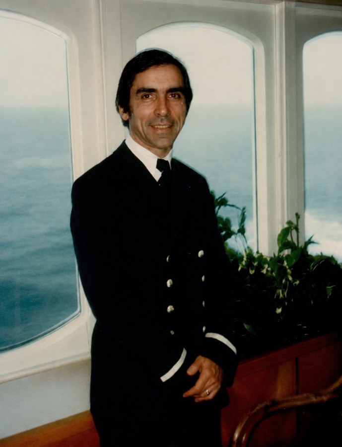 Arlindo Veríssimo Codinha in his merchant-navy uniform aboard a ship, the Atlantic behind him.